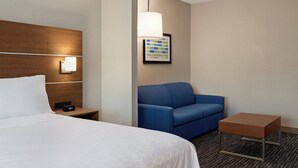 Una habitación de hotel con una cama, una mesita de noche, un sofá azul, una pequeña mesa y una lámpara de pared.
