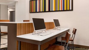Una moderna zona de recepción de hotel con tres computadoras de escritorio, un mostrador de madera y un cuadro abstracto colorido en la pared.