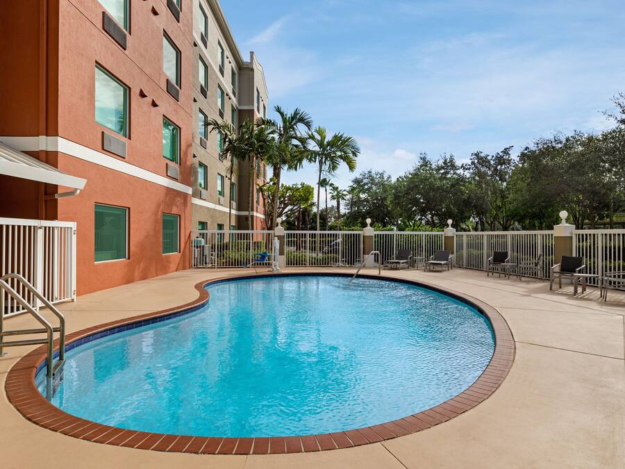 A swimming pool with a brick border, surrounded by a white fence and palm trees.