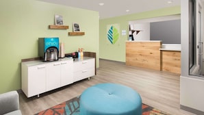 A modern hotel room with a kitchenette, a blue ottoman, and a colorful rug. - WoodSpring Suites McKinney (McKinney)