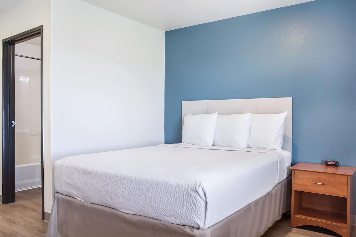 A neatly made bed with white linens, a wooden nightstand, and a blue accent wall.