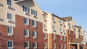 A multi-story hotel with a brick facade, multiple windows, and a covered entrance. - WoodSpring Suites McKinney (McKinney)