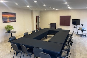 Une salle de conférence avec une longue table, des chaises, un téléviseur, une plante et un tableau accroché au mur.