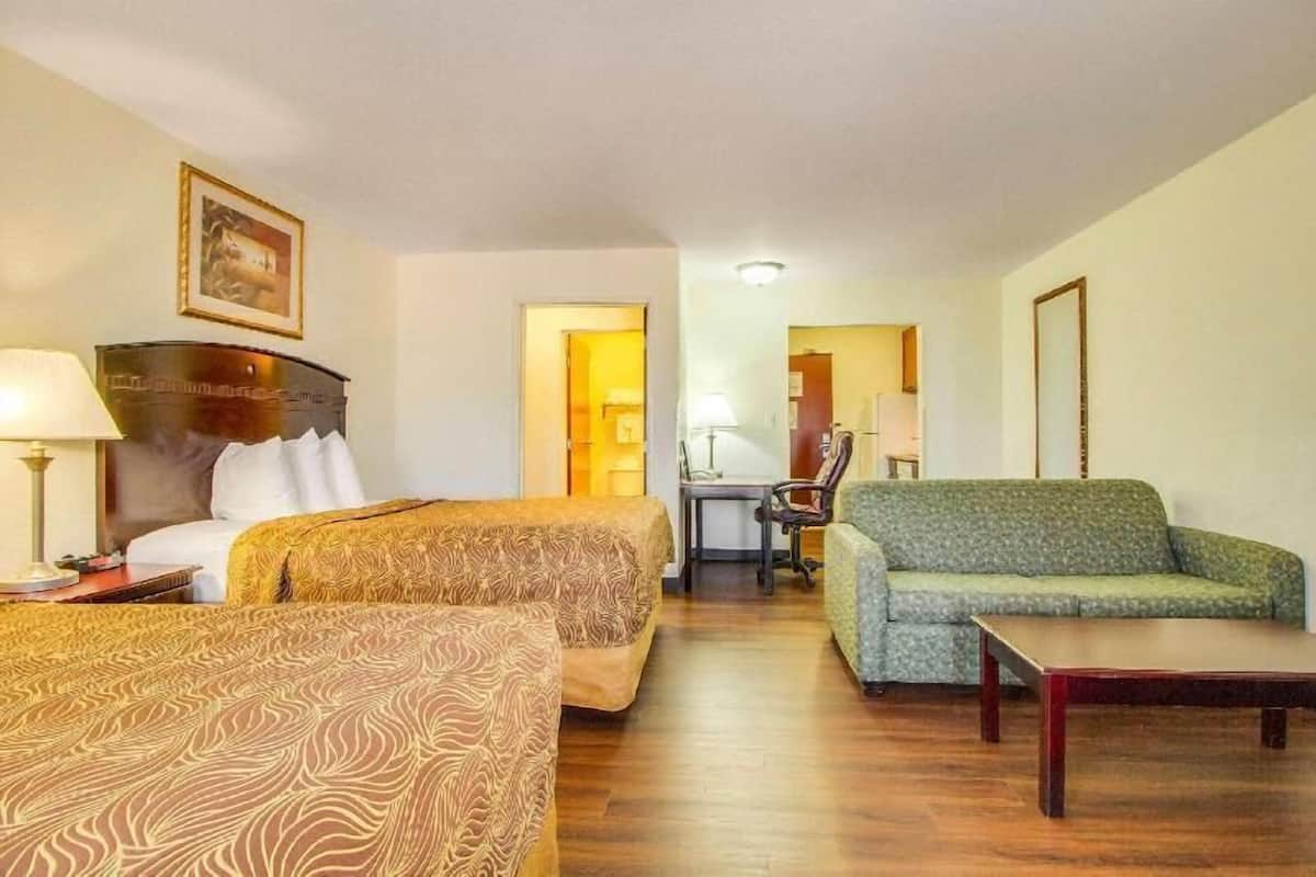 A hotel room with two beds, a green sofa, a wooden table, and a desk with a chair.