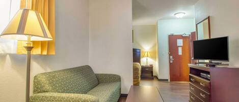 Ein Hotelzimmer mit einer Couch, einem kleinen Tisch, einem Fernseher und einem Schminktisch.