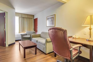 A hotel room with a wooden floor, a sofa, a chair, a small table, a lamp, and a framed picture on the wall.