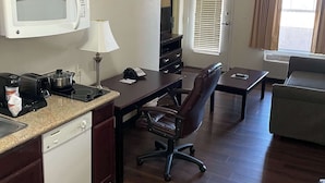 A compact kitchen with a microwave, toaster, and coffee maker, a small dining table with a chair, and a sofa in a living area with a window. - MainStay Suites Texas Medical Center/Reliant Park (Houston)