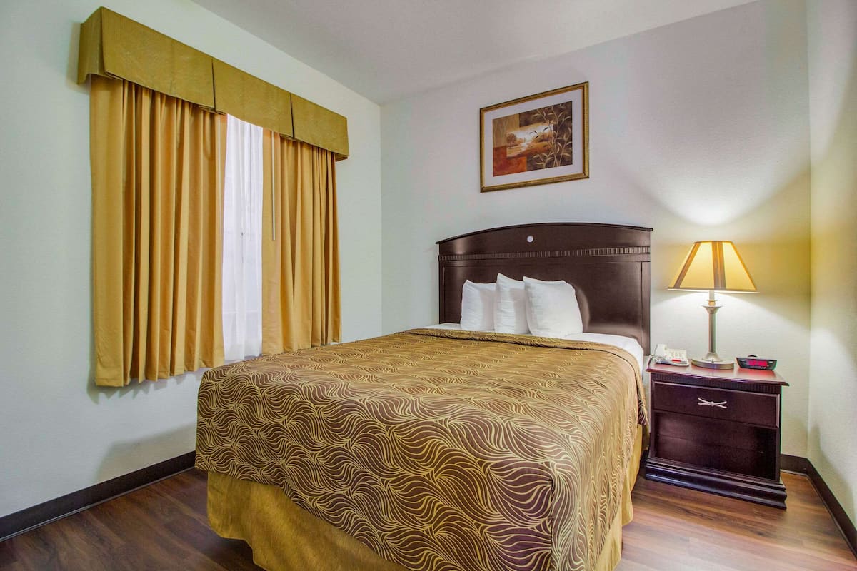 A hotel room with a bed, a nightstand, a lamp, and a painting on the wall.
