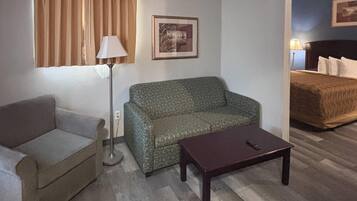 A room with a sofa, a small table, a lamp, a bed, and a framed picture on the wall.