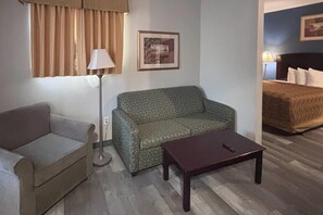 Una habitación con sofá, una mesita, lámpara, cama y un cuadro en la pared.