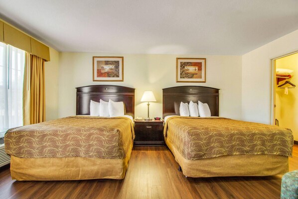 A hotel room with two beds, a nightstand with a lamp, and two framed pictures on the wall.