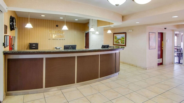 A hotel reception area with a curved counter, pendant lighting, and a sign indicating 'MainStay Suites by Choice Hotels'. - MainStay Suites Texas Medical Center/Reliant Park (Houston)