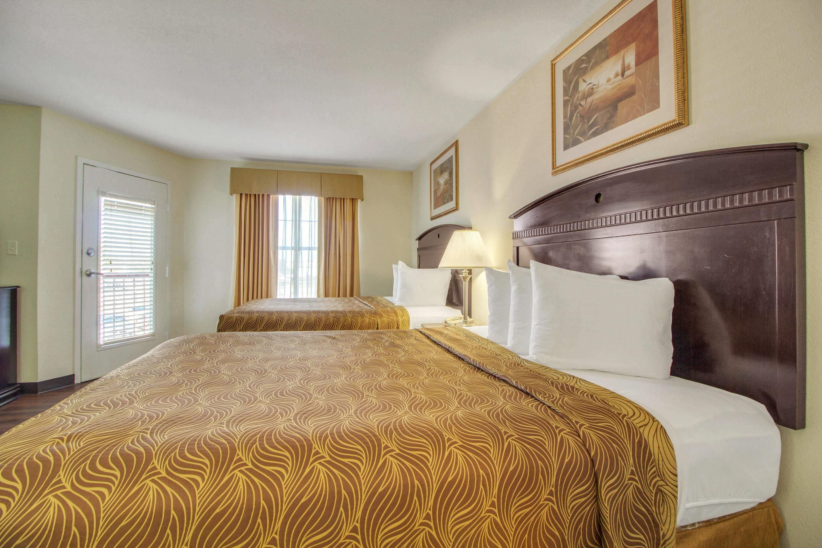 A hotel room with a large bed, a bedside table with a lamp, a window with curtains, and a painting on the wall.