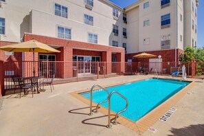 A swimming pool with a metal safety railing, a sun umbrella, and a fenced patio area with outdoor seating.