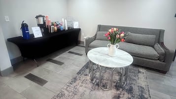 A reception area with a black counter, a grey sofa, and a round table with a vase of flowers.