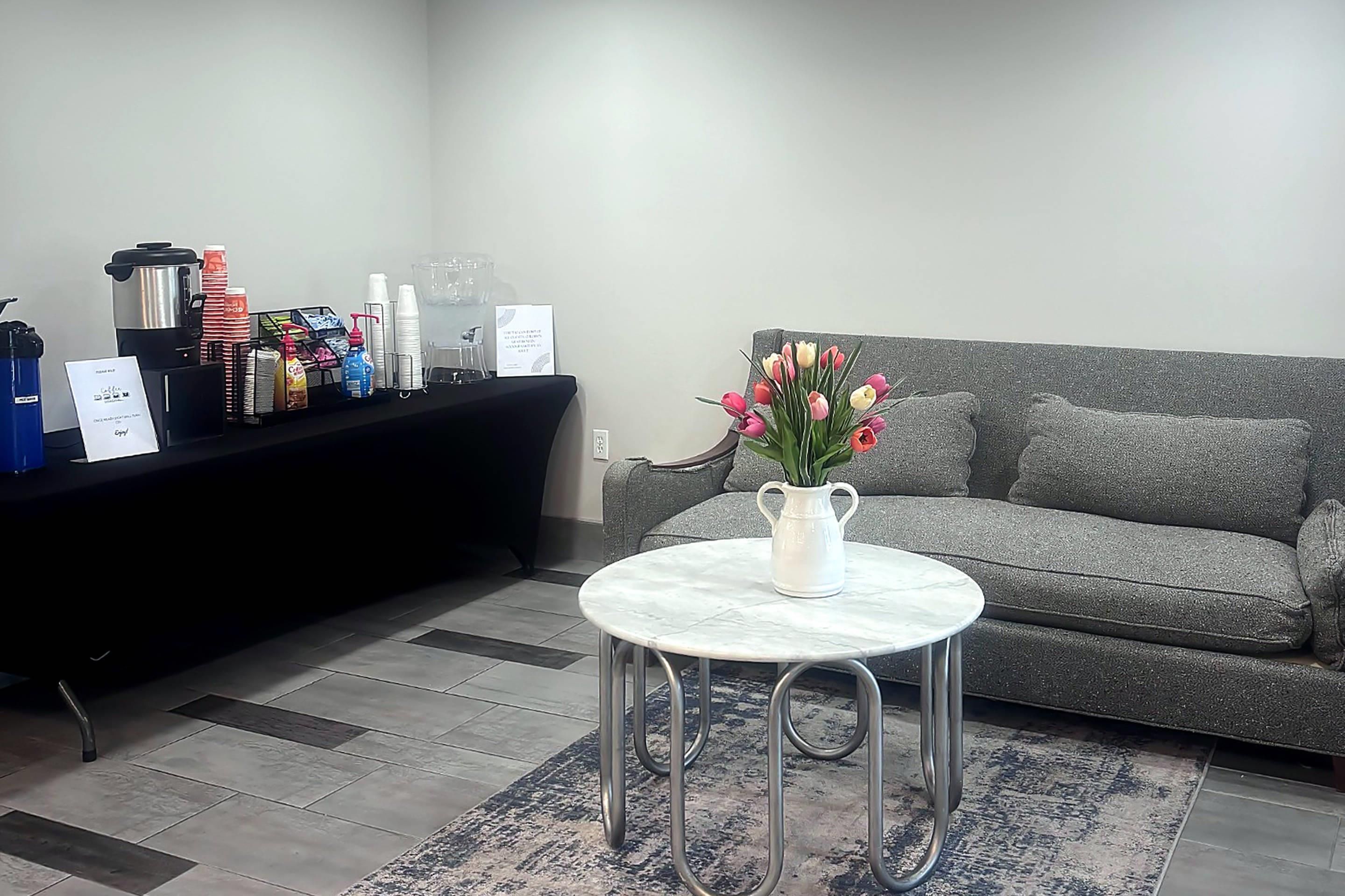 A reception area with a coffee station, a sofa, and a small table with a vase of flowers.