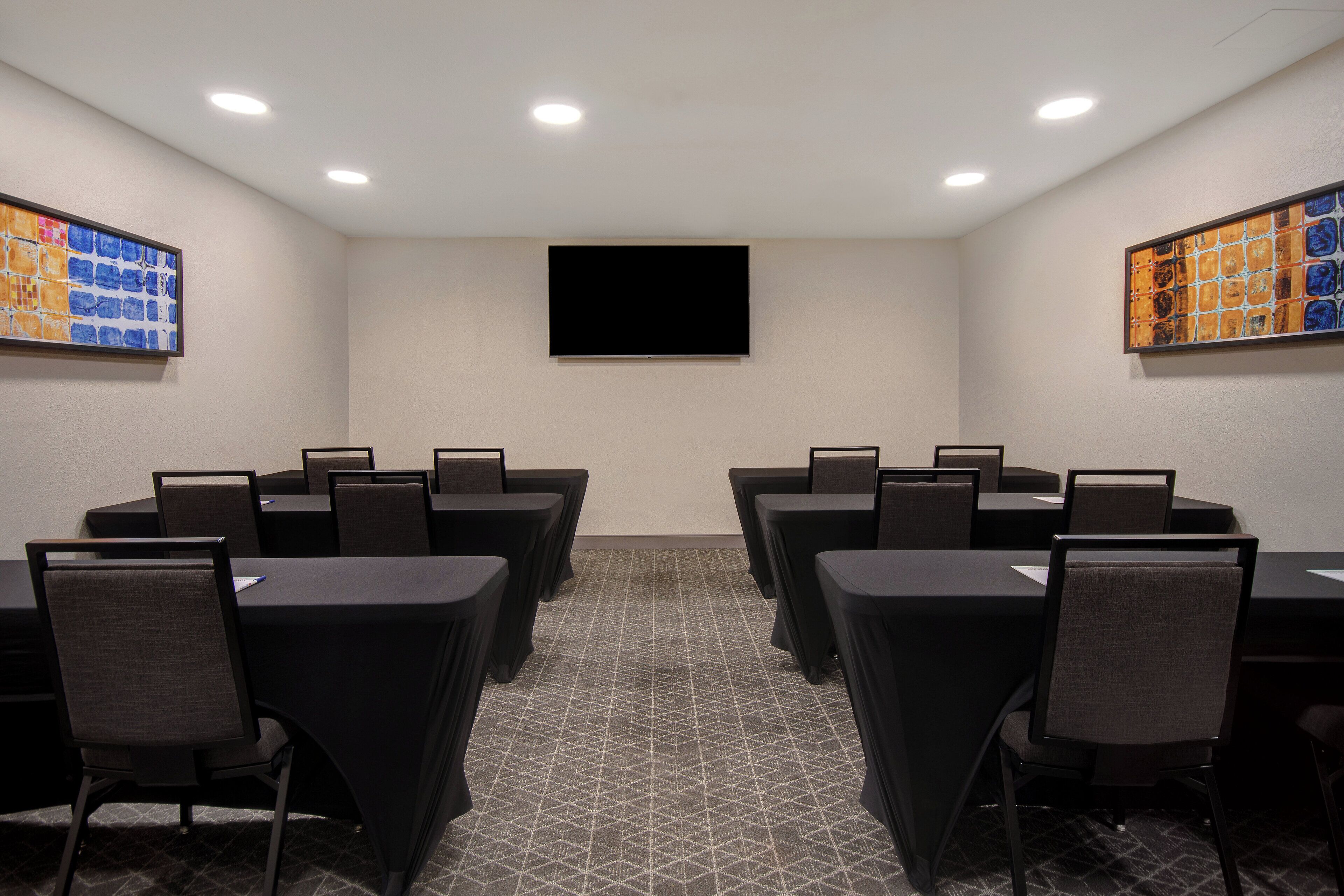 A conference room with a flat-screen TV, multiple tables with chairs, and patterned carpet.
