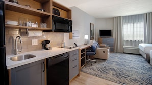 A modern hotel room with a kitchenette, a flat-screen TV, a bed, and a view of the city.