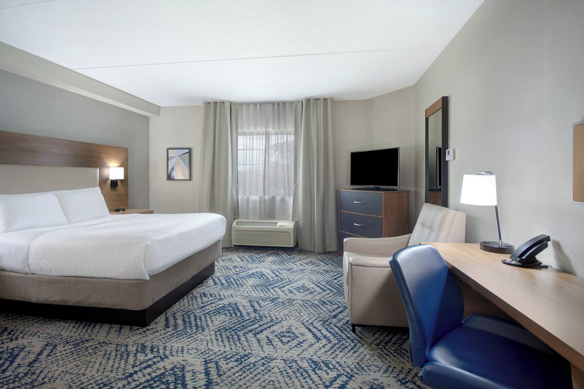 Habitación de hotel con cama, escritorio, silla, televisión y ventana con cortinas.