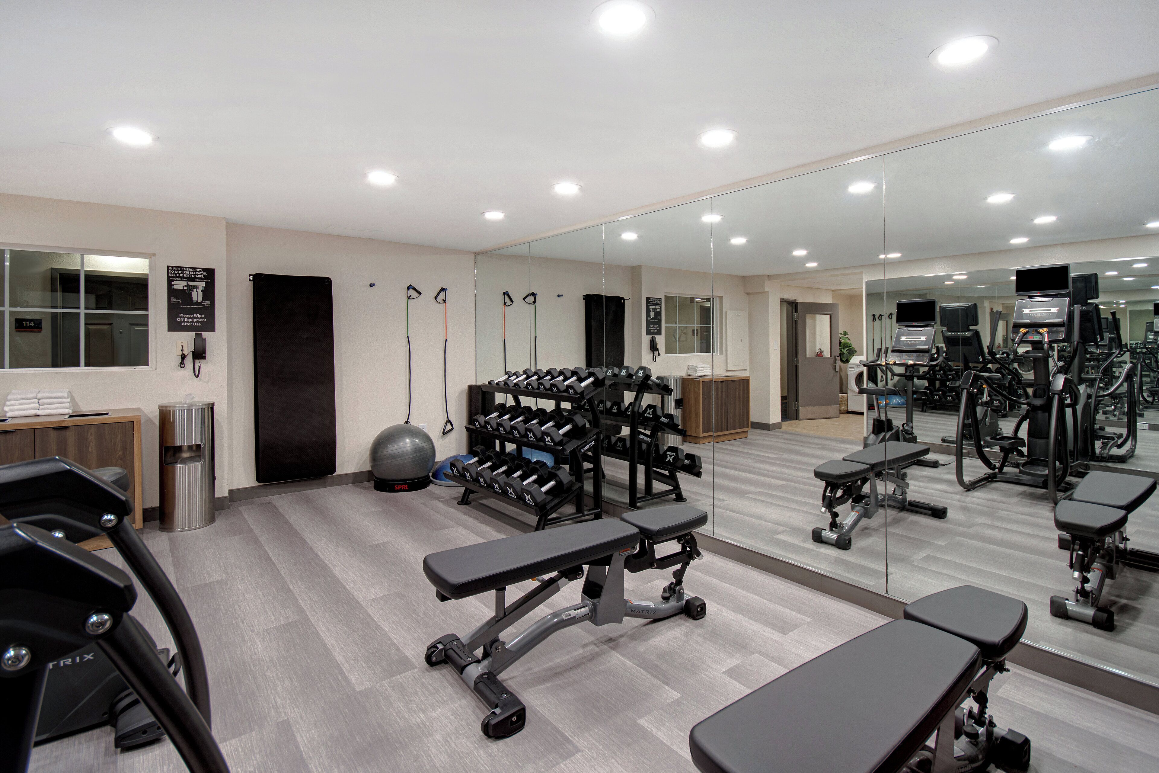 A gym with exercise equipment, benches, and a mirrored wall.