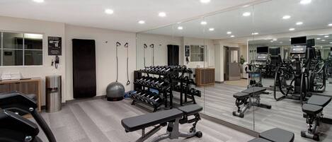 A gym with exercise equipment, benches, and a mirrored wall.
