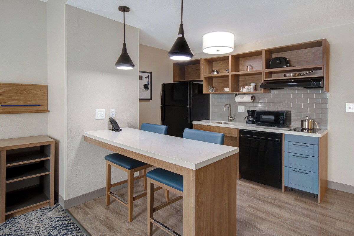 A modern kitchen with a central island, wooden cabinets, a black refrigerator, a microwave, and a dishwasher.