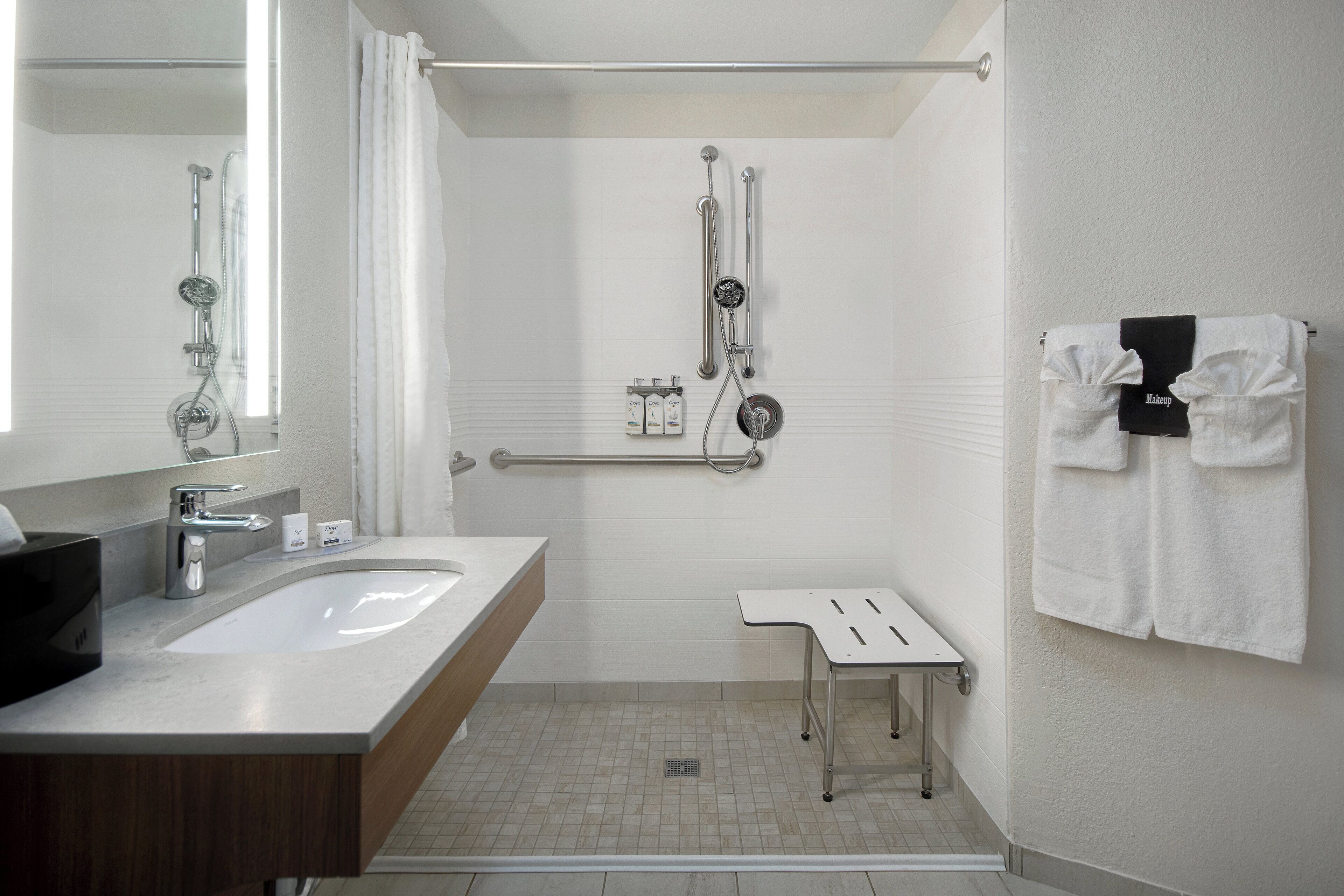 Une salle de bain moderne avec un grand lavabo, une douche équipée de barres d’appui et une petite table.