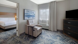A hotel room with a bed, a seating area, a television, and a window with curtains.