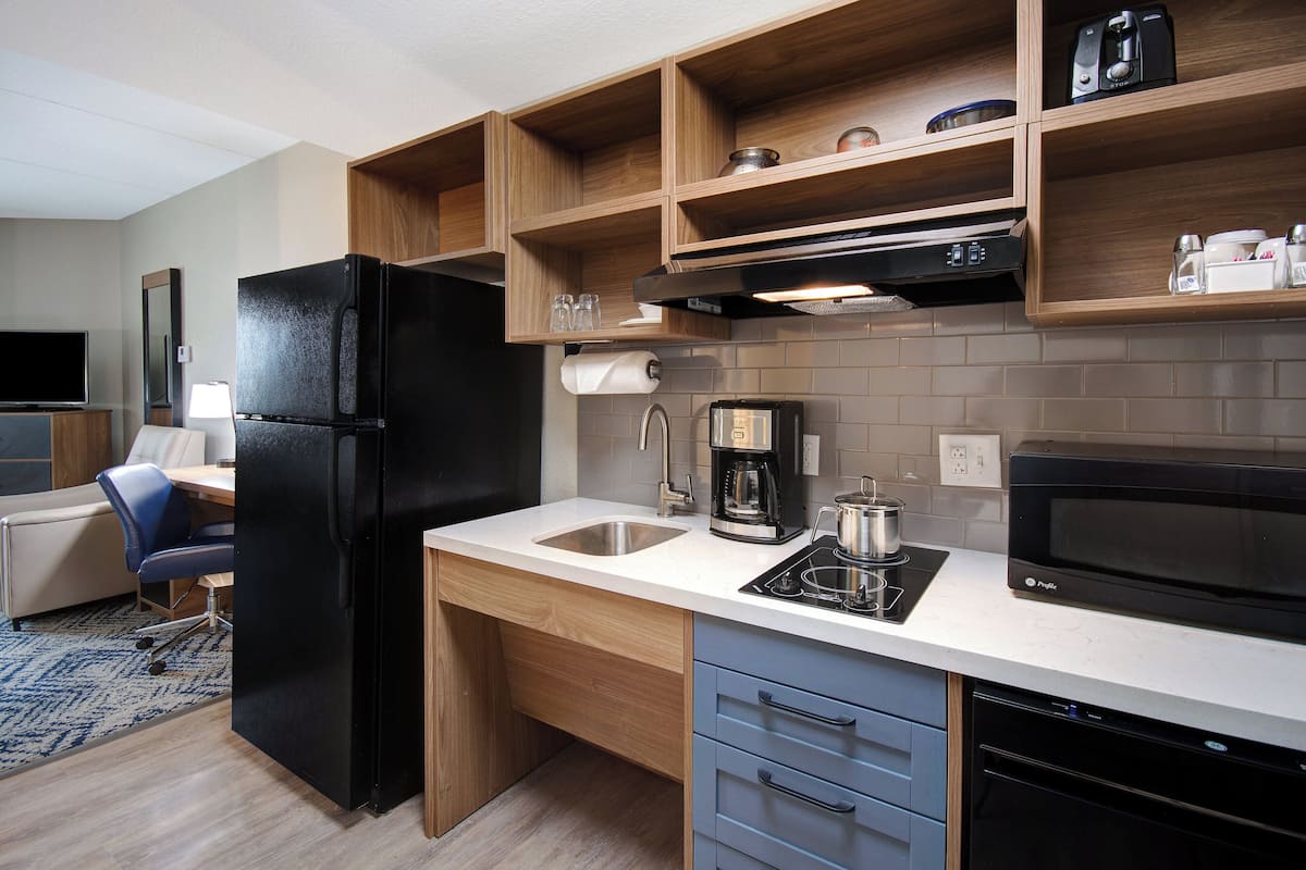 Cocina compacta con refrigerador negro, microondas, cafetera y pileta.