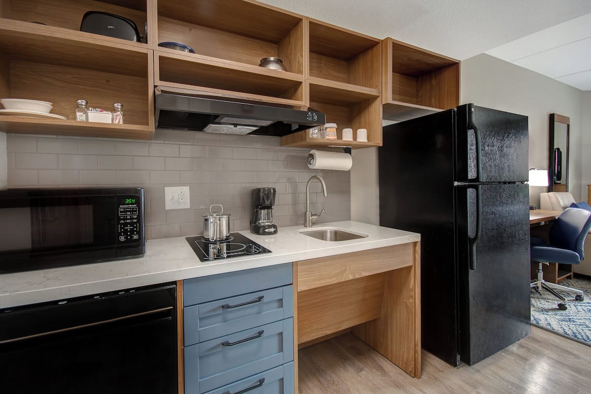 Una cocina moderna con un refrigerador negro, un microondas, una cafetera y estantes de madera.
