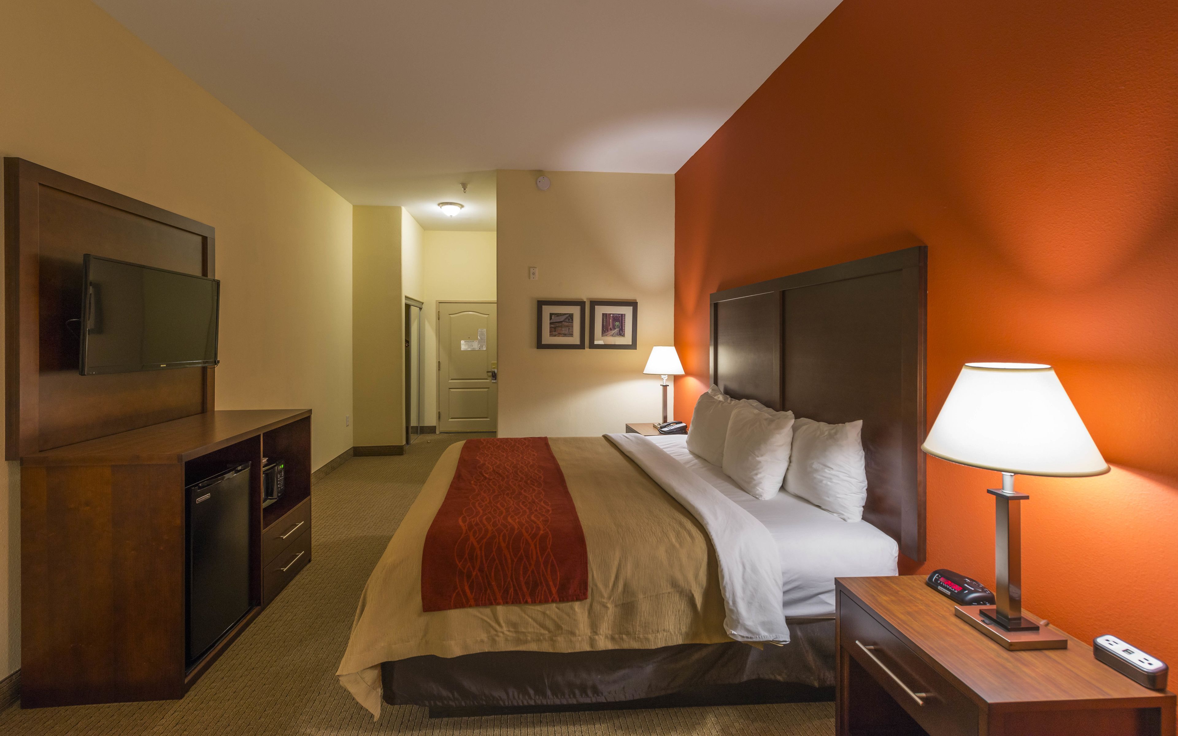 Ein Hotelzimmer mit Bett, Nachttisch, Lampe, Fernseher und einem Schreibtisch mit Computer.