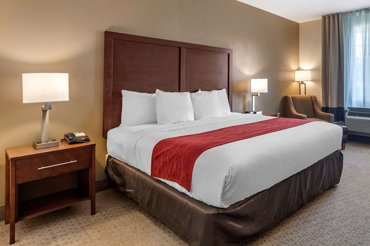 A hotel room with a large bed, two bedside tables, a chair, and a window with curtains.
