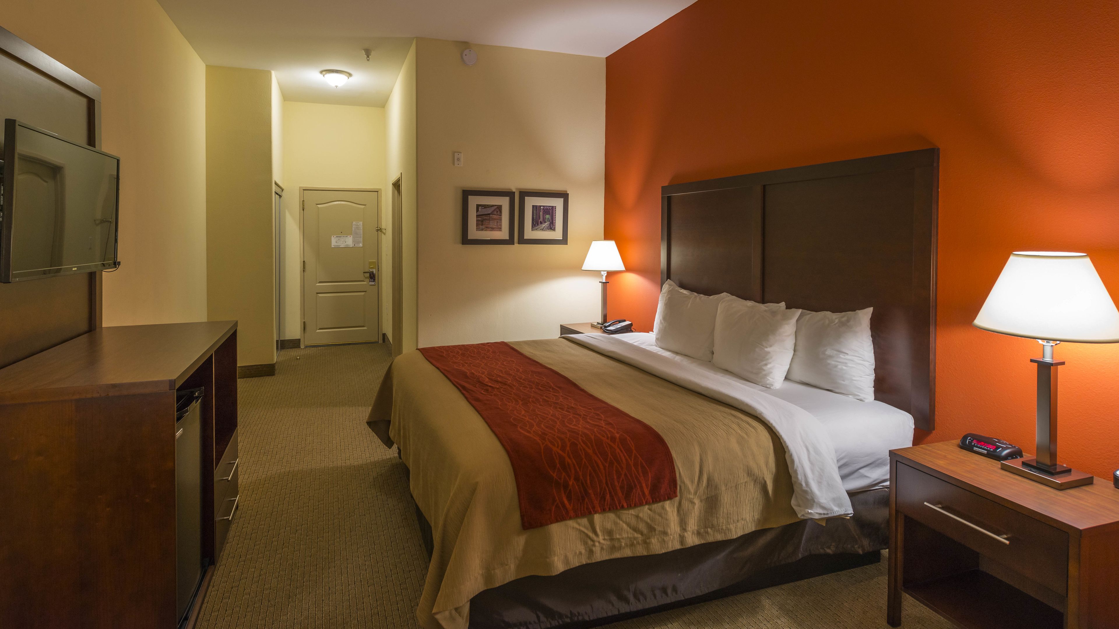 Quarto de hotel com cama, abajures, escrivaninha e televisão.