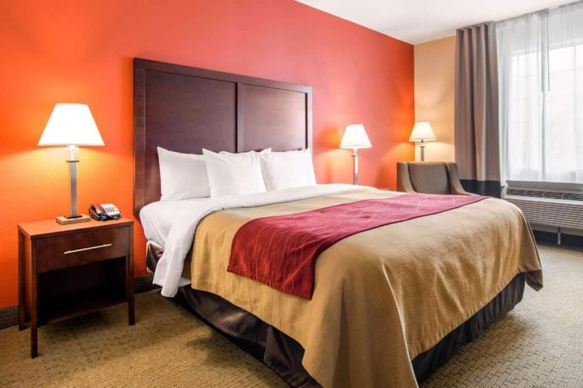 A hotel room with a bed, two bedside tables, a chair, and a window with curtains.