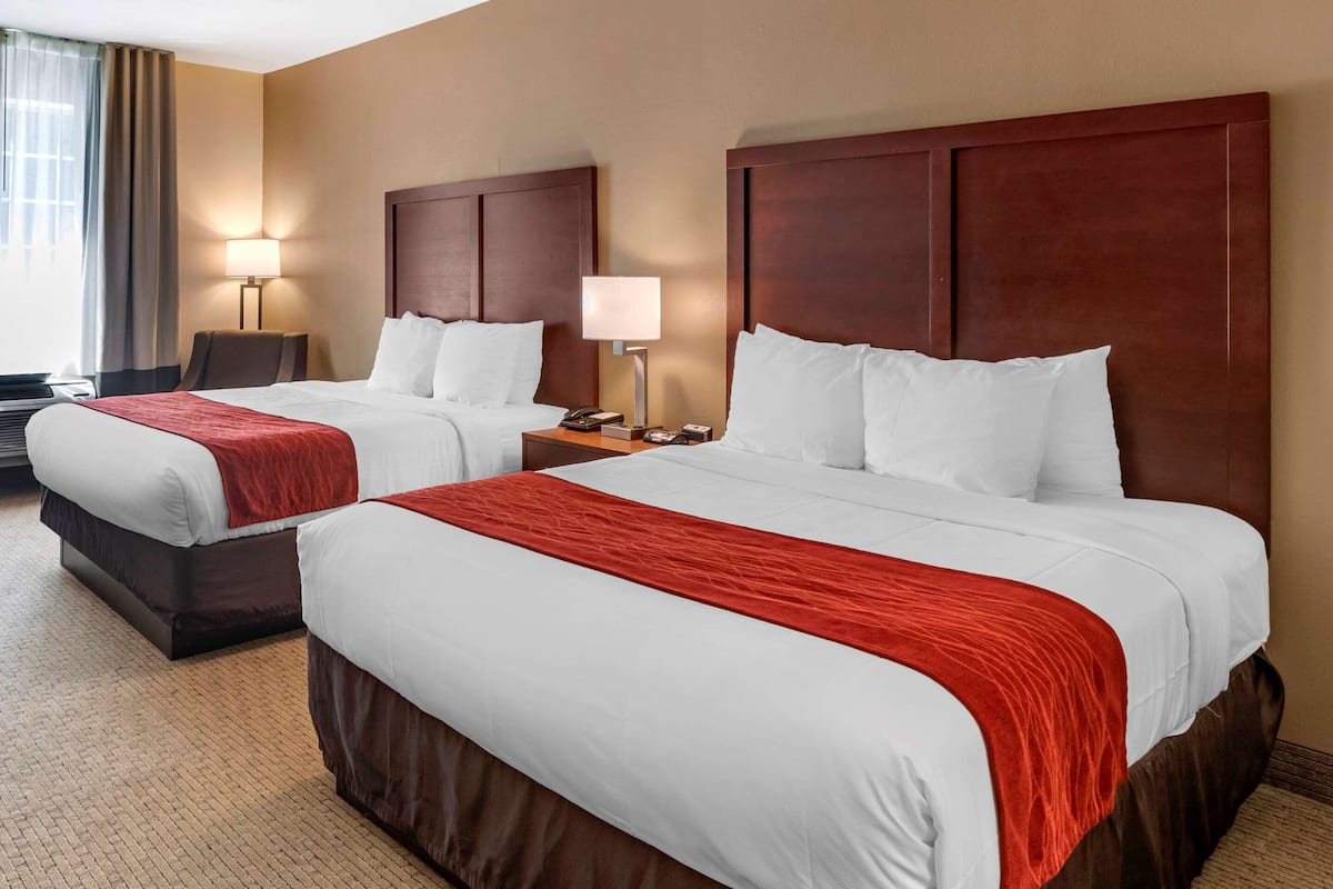 A hotel room with two beds, each with a red blanket, wooden headboards, and bedside lamps.