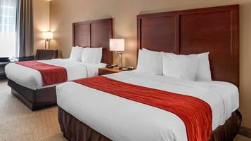 Habitación de hotel con dos camas, cada una con una manta roja, cabeceros de madera y lámparas de noche.