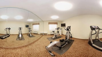 Un gimnasio con varias máquinas de ejercicio, un espejo grande y alfombra estampada.