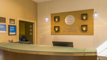 A reception desk with a glass top, a wooden wall with a sign for Comfort Inn & Suites, and framed certificates on the wall.