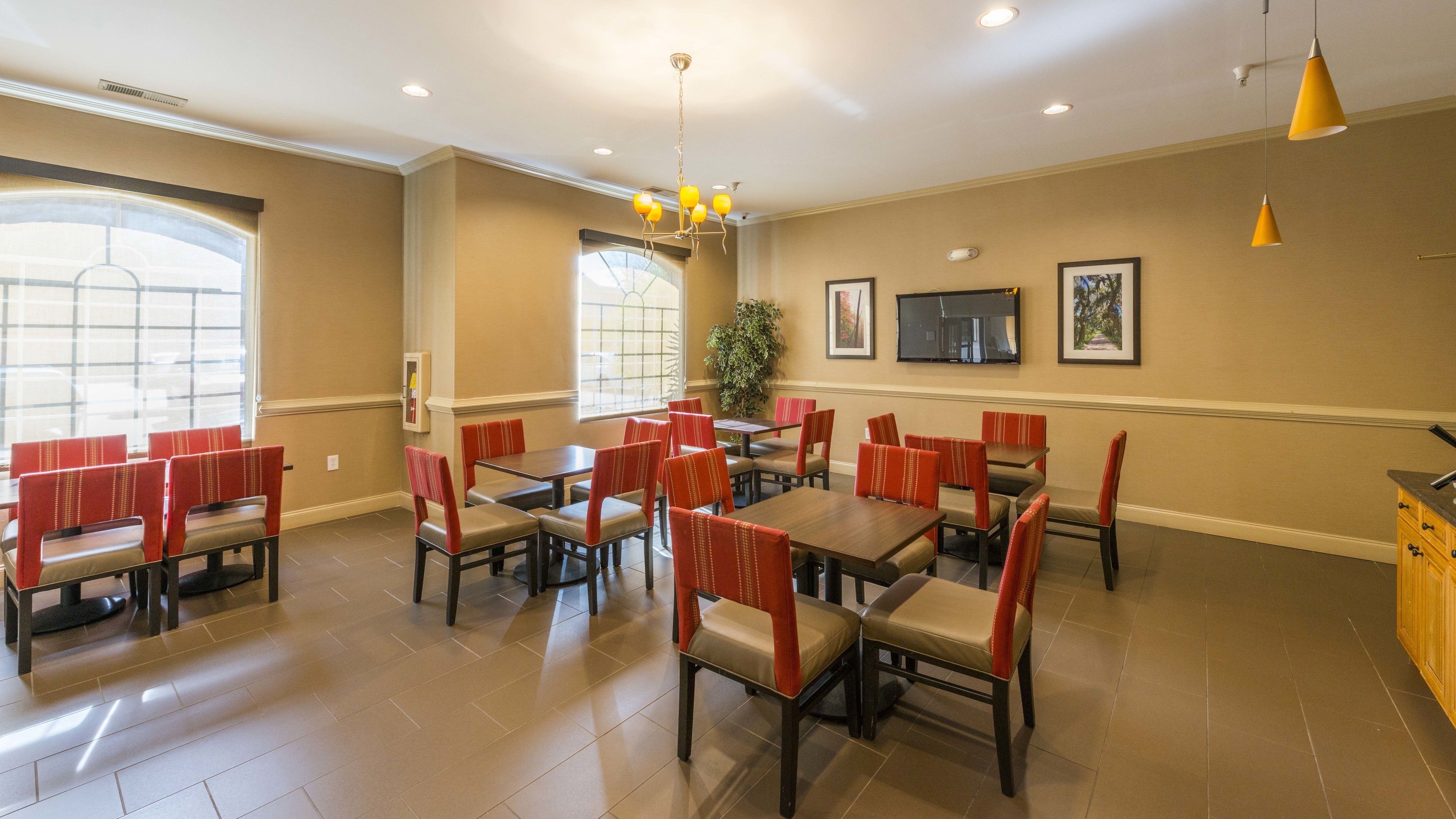 A dining area with multiple tables and chairs, a large window, and a television on the wall.
