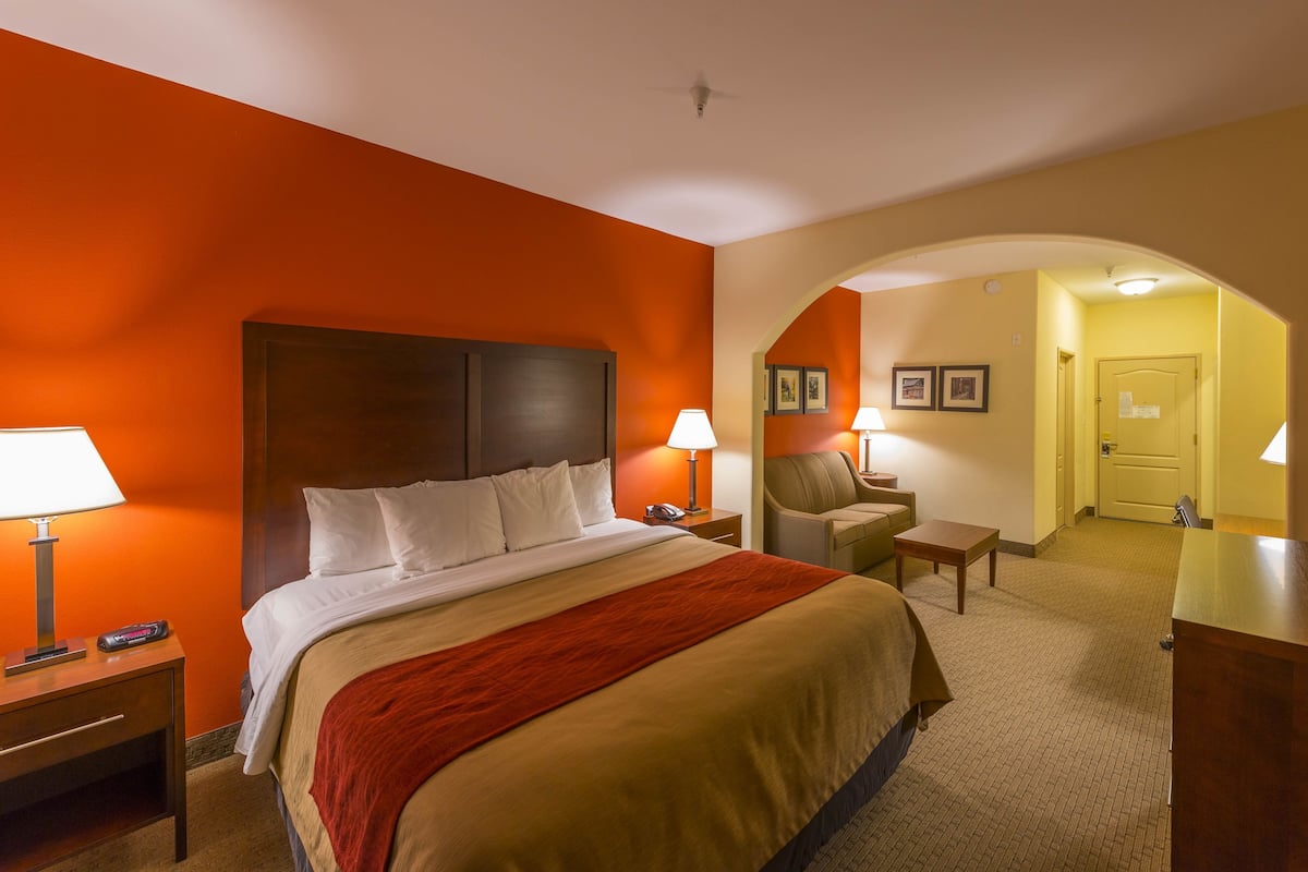 A hotel room with a bed, a desk, a chair, and an arched doorway leading to another room.