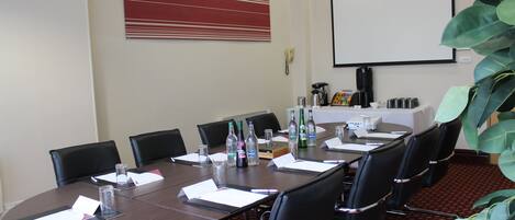 Ein Konferenzraum mit langem Tisch, Stühlen, einer Projektionsleinwand und einer Kaffeestation.
