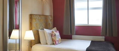 A hotel room with a bed, bedside lamp, and a window with curtains.