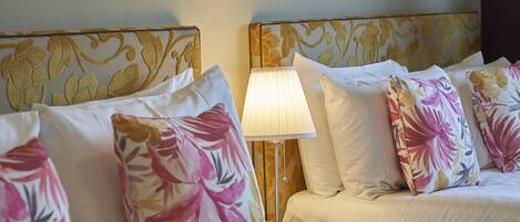 Habitación de hotel con dos camas, cada una con almohadas de estampado floral y cabeceros con diseño de pan de oro.