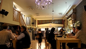 Interior de restaurante com mesas e cadeiras de madeira, área de bar e escadaria para um andar superior.