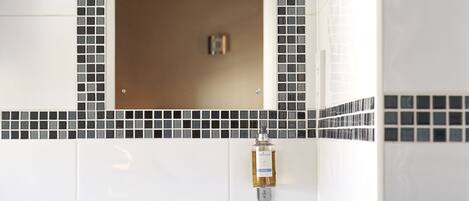 A bathroom with a white sink, a mirror with a black and white mosaic border, and a wooden vanity.