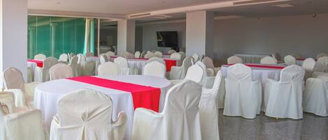 A banquet hall with round tables, white chairs, and red tablecloths.
