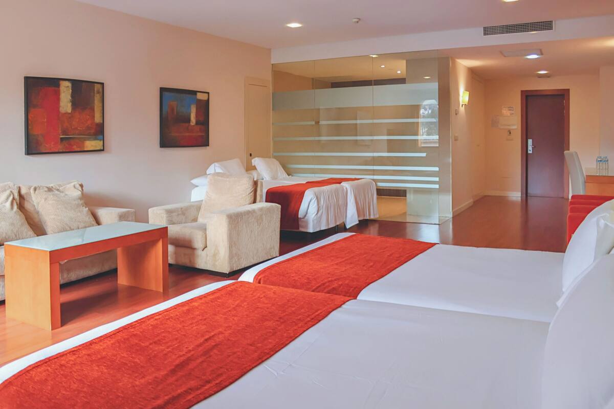 A hotel room with a bed, a sofa, a chair, a table, and artwork on the walls.