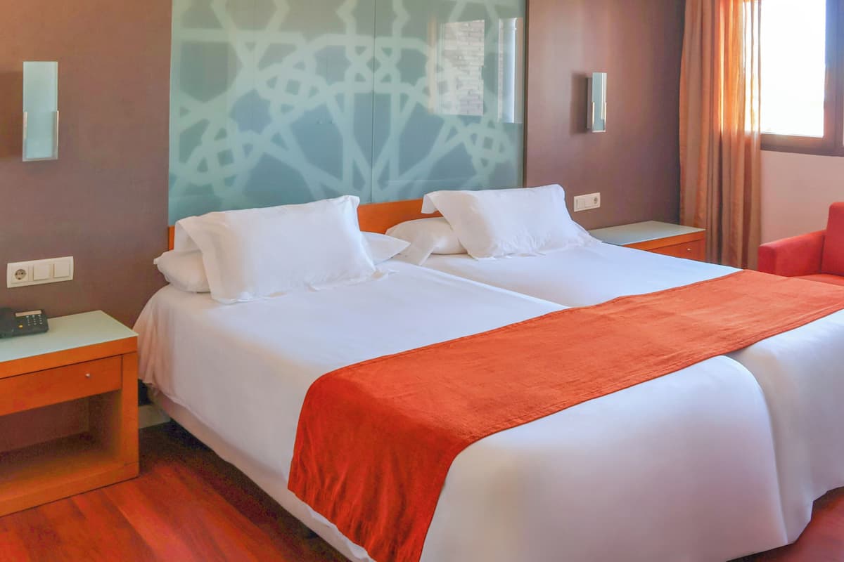 A hotel room with two beds, a red chair, a telephone, and a wall with a geometric pattern.
