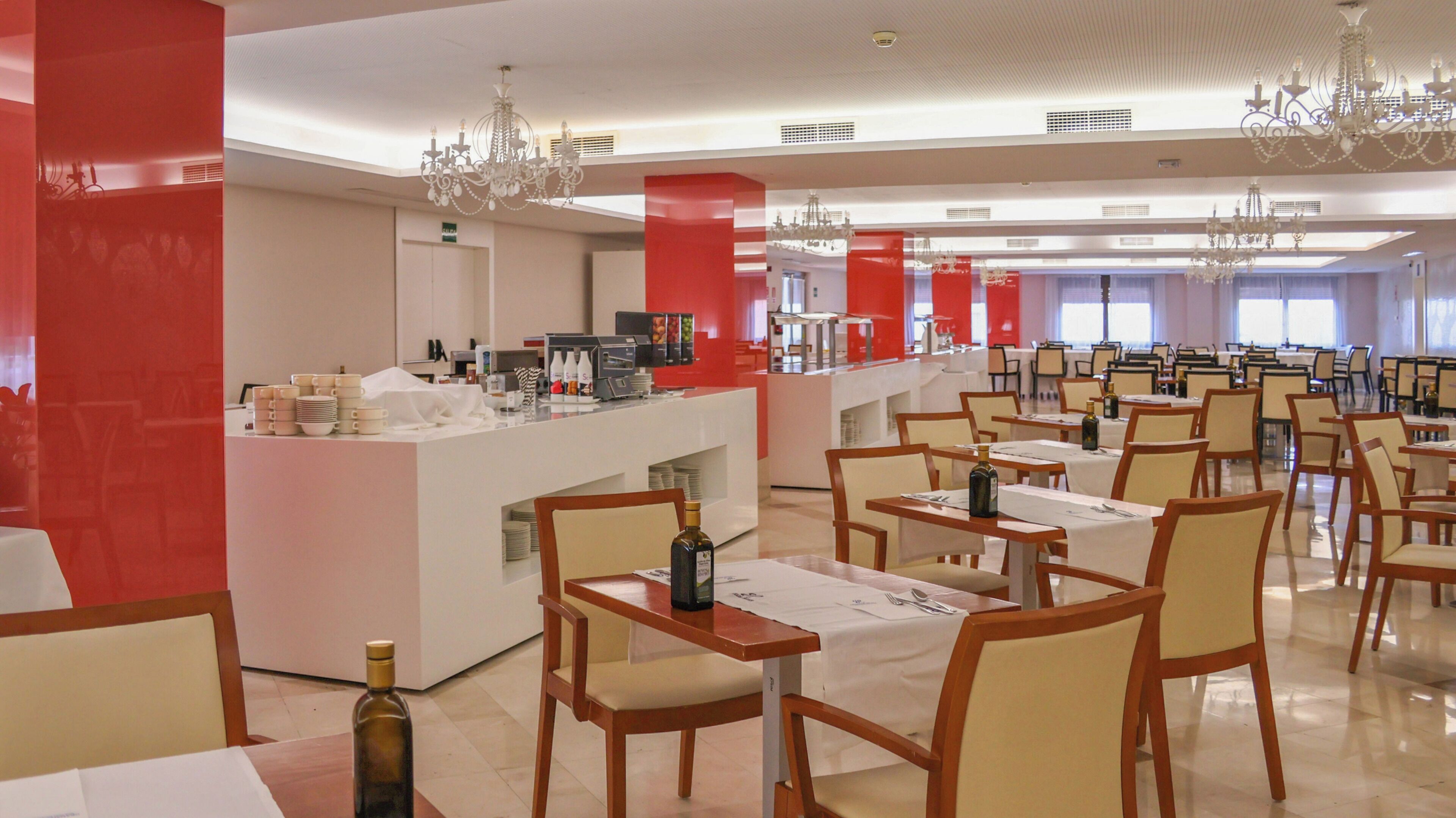 Un comedor amplio con varias mesas y sillas, una barra central con estación de bebidas y candelabros decorativos.