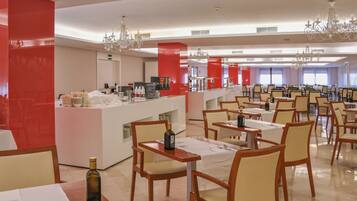 Un comedor amplio con varias mesas y sillas, una barra central con estación de bebidas y candelabros decorativos.